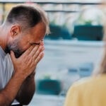 A man covering his face with his hands while talking with a support worker