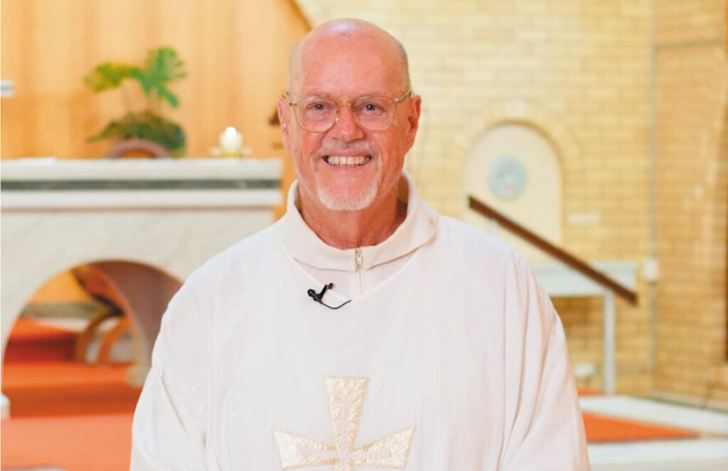 A smiling retired priest in white vestments in a church