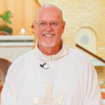 A smiling retired priest in white vestments in a church
