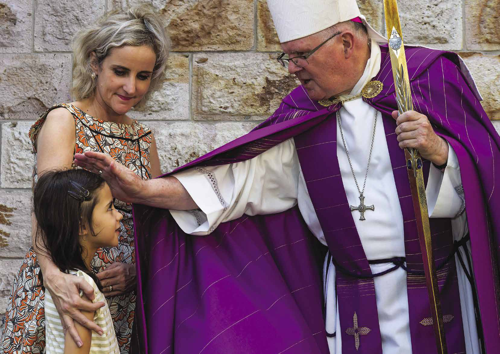 A bishop in purple vestments blessing a young girl and her mother