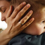 A mother holding her young son close, her hand cradling his head